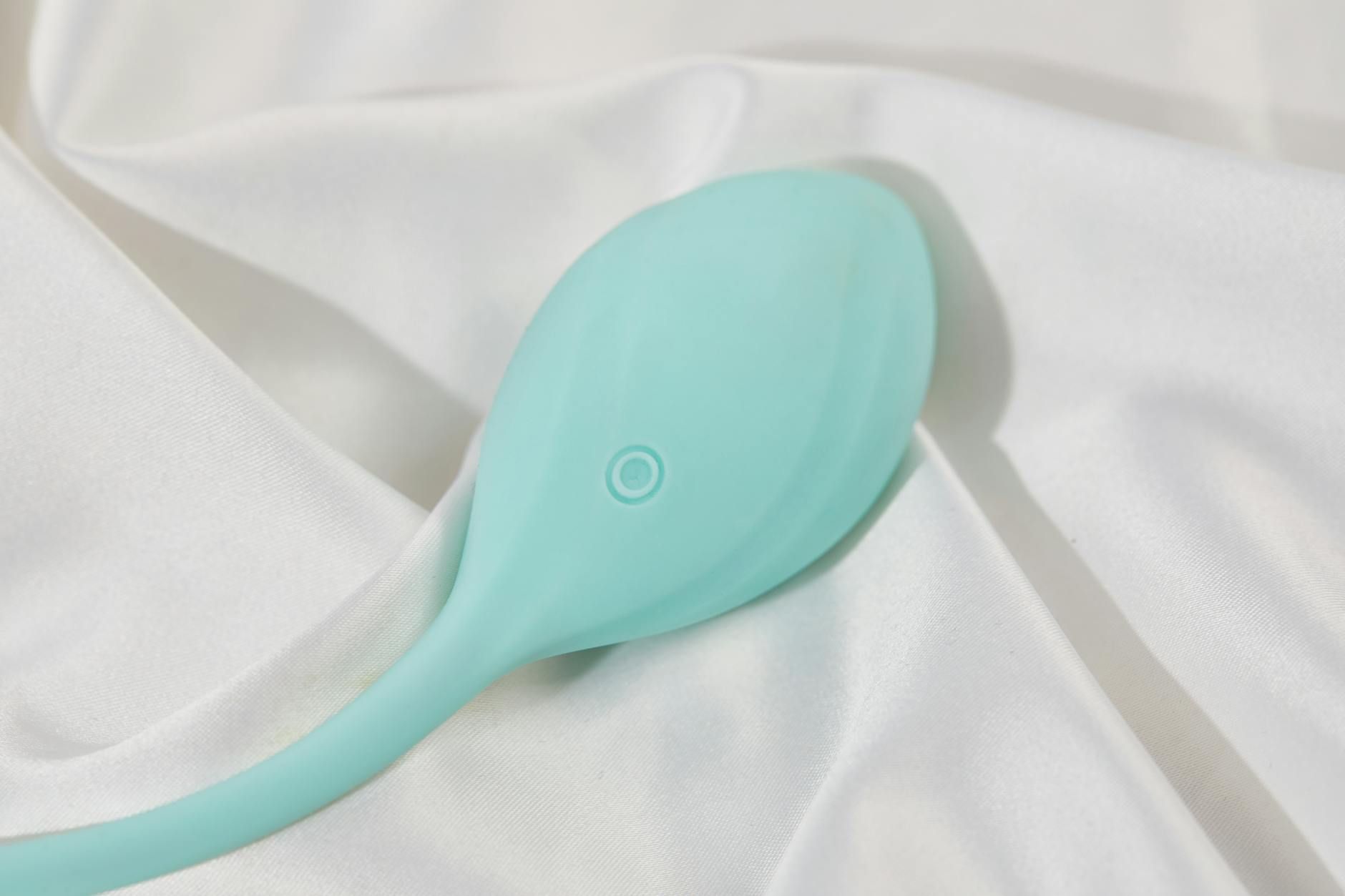 A sleek teal lemon vibrator on white silk fabric, ready for intentional self-pleasure