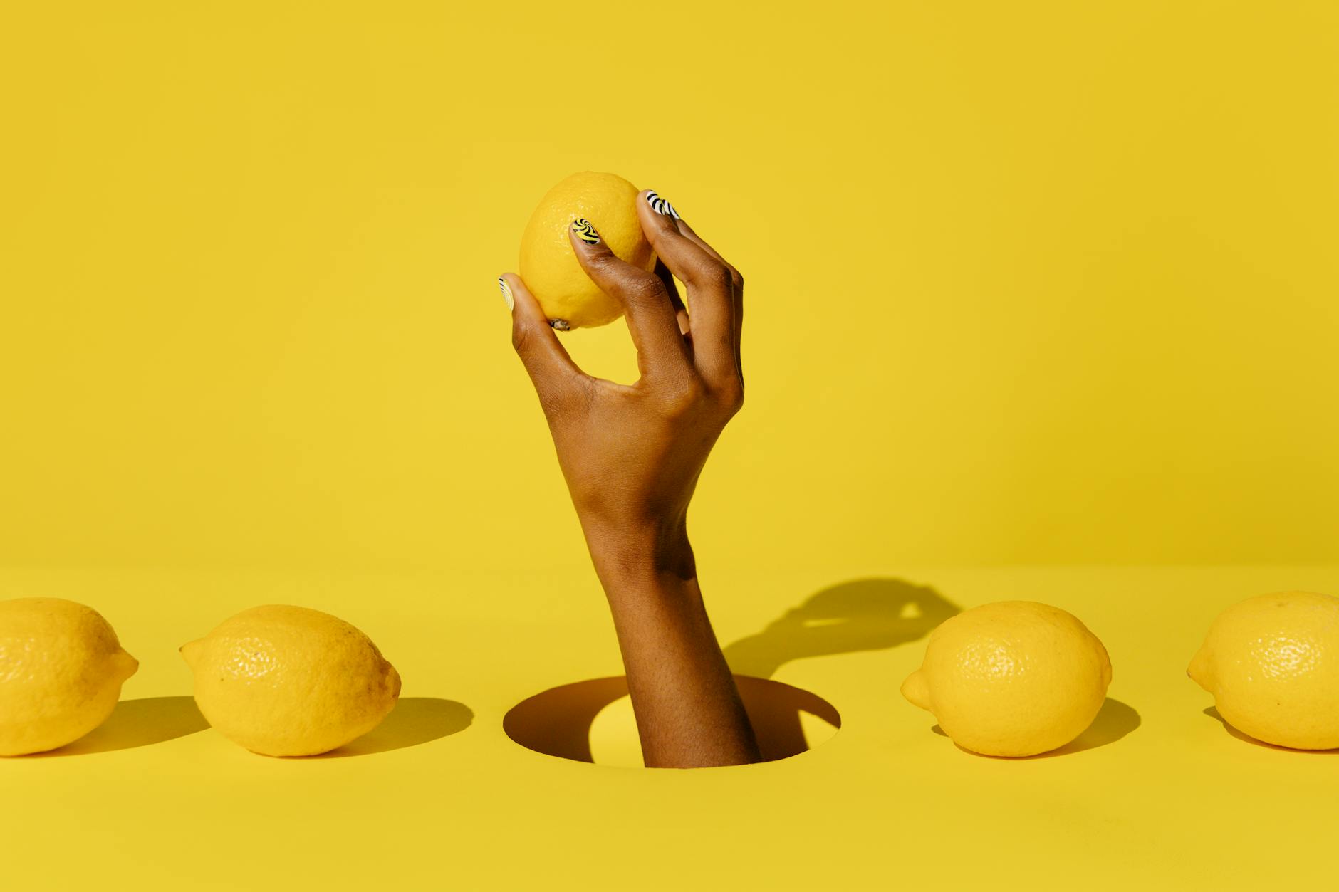 Hand holding a fresh lemon against a bright yellow background, symbolizing gentle, natural approaches to post-surgery pleasure
