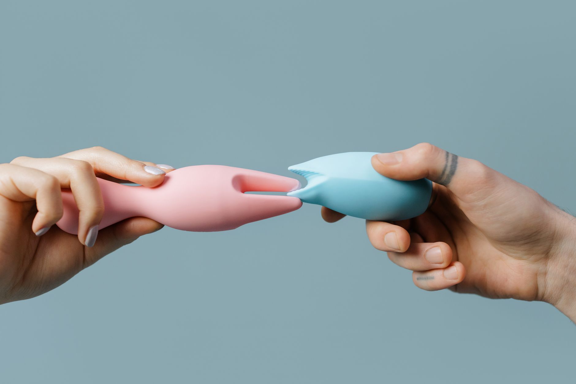 Woman holding blue and pink clitoral vibrators with thoughtful expression