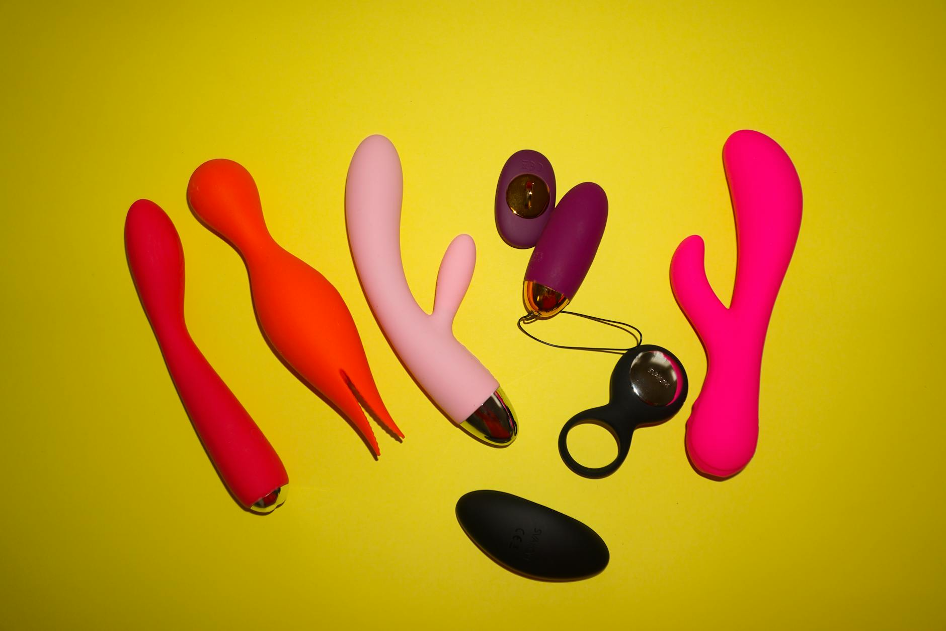 Colorful sex toys arranged on a bright yellow background, showcasing various vibrator designs and shapes